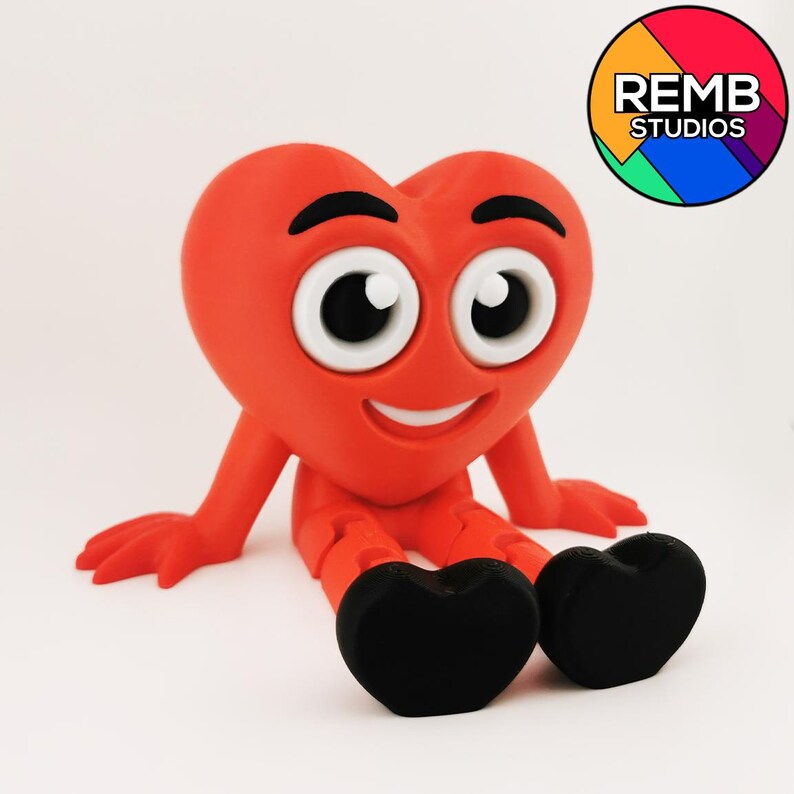 Puede incluir: Un personaje rojo en forma de coraz&oacute;n con una cara sonriente y ojos grandes est&aacute; sentado con las piernas cruzadas. El personaje tiene pies en forma de coraz&oacute;n negros.