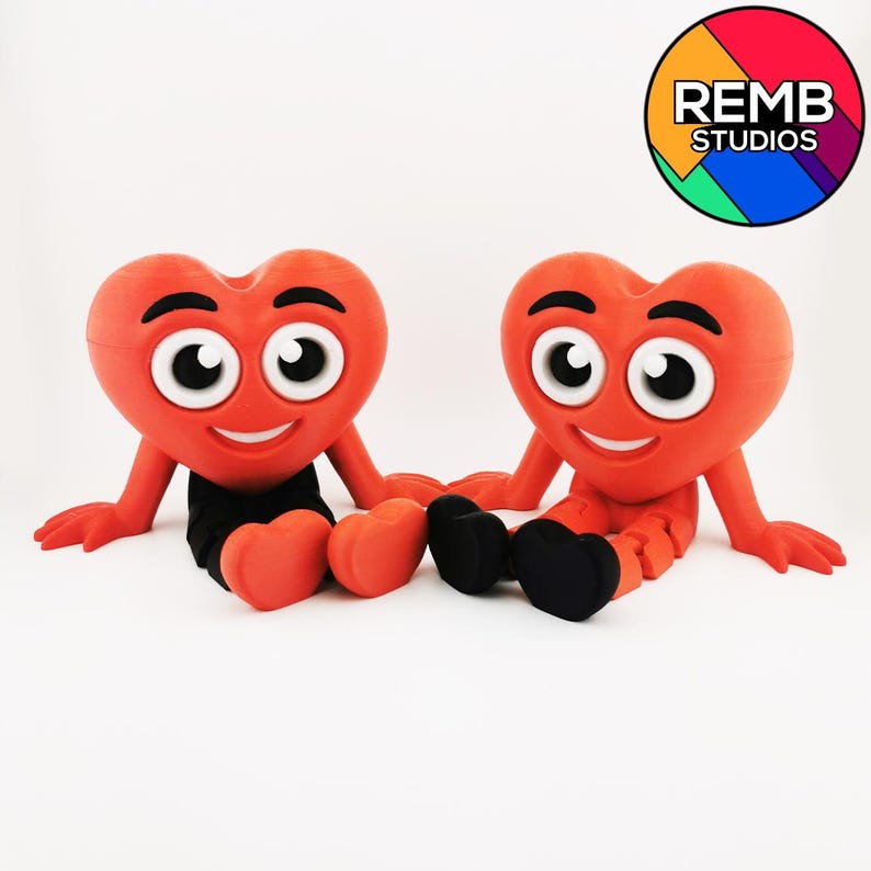 Puede incluir: Dos figuras rojas en forma de coraz&oacute;n con caras sonrientes y ojos grandes. Est&aacute;n sentados con las piernas cruzadas y llevan pantalones negros. Las figuras est&aacute;n hechas de un material suave y flexible y tienen un aspecto juguet&oacute;n y de dibujos animados.