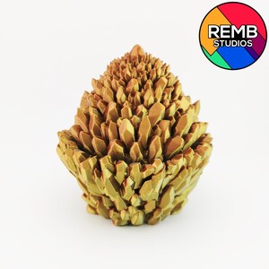 May include: A golden-colored, crystalline sculpture with a textured surface. The sculpture is composed of numerous pointed, geometric shapes clustered together, resembling a geode or a cluster of crystals. The REMB STUDIOS logo is in the upper right corner.
