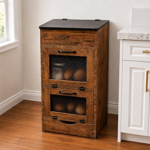 May include: A rustic wooden storage cabinet with a black top and metal mesh doors. The cabinet has two compartments with black handles and a drawer. The cabinet is designed for kitchen storage.