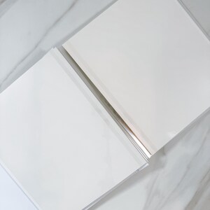 two white rectangular books lying on a marble surface.