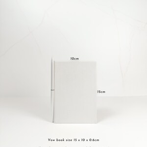 A white pen is placed next to a small white notebook on a white surface.