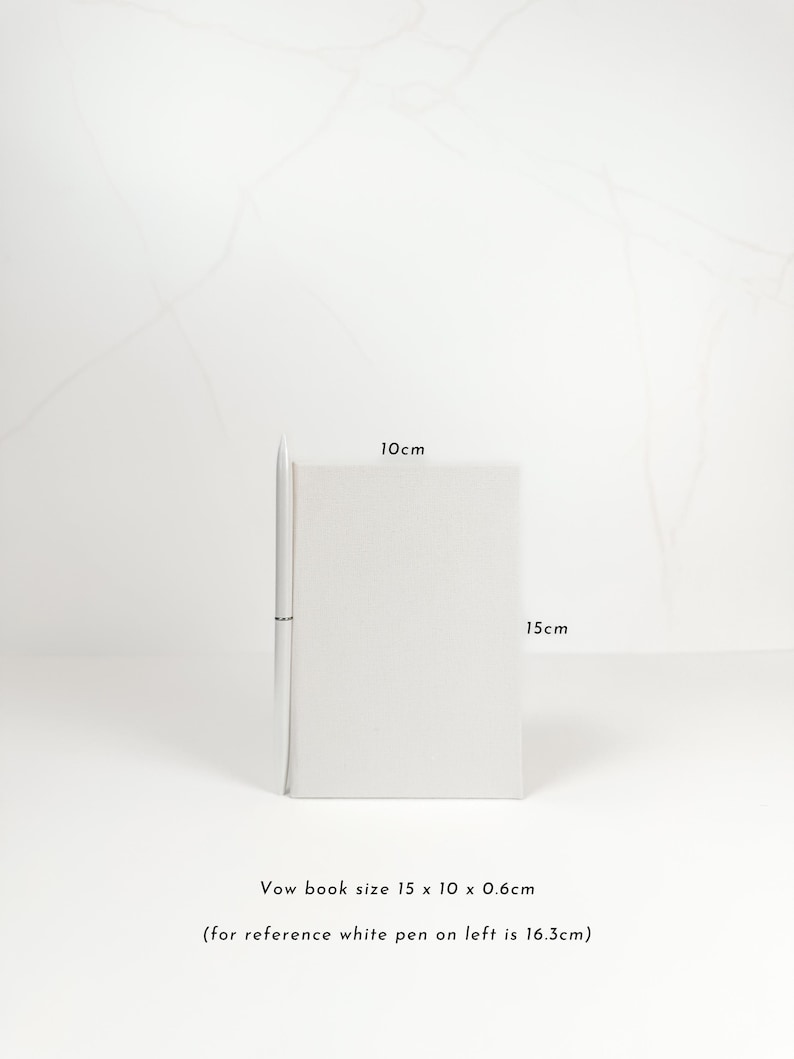 A white pen is placed next to a small white notebook on a white surface.