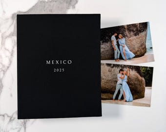 Könnte beinhalten: Ein schwarzes Fotoalbum mit dem in Weiß aufgedruckten Text MEXICO 2025 auf dem Einband. Rechts neben dem Album liegen zwei rechteckige Fotos, die jeweils ein Paar an einem Strand in der Nähe einer großen Felsformation zeigen.