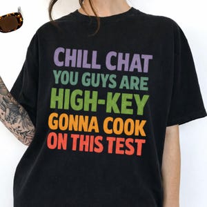 May include: Black t-shirt with the text "CHILL CHAT YOU GUYS ARE HIGH-KEY GONNA COOK ON THIS TEST" in purple, green, orange, and red. The shirt is a relaxed fit and has a vintage look.