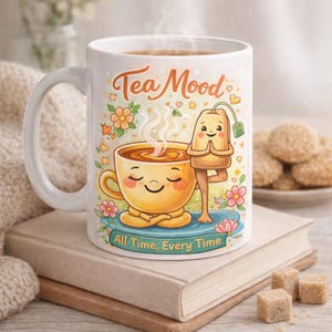 Op de afbeelding: Witte keramische mok met de tekst "Tea Mood" en een cartoonillustratie van een theekopje en een theezakje in yogahoudingen. De mok heeft de tekst "All Time, Every Time" en is versierd met bloemen.