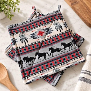 May include: Two square quilted pot holders featuring a repeating pattern of black horses in motion, dreamcatchers, and geometric bands in red, gray, and white. Each pot holder includes a small fabric loop at the corner for convenient hanging storage.
