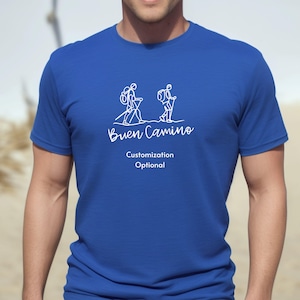 May include: A royal blue t-shirt with a white outline of two people hiking with backpacks and walking sticks. The text "Buen Camino" is printed below the image. The text "Customization Optional" is printed below the text.