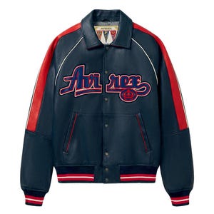 Puede incluir: Chaqueta de cuero azul marino con detalles rojos en las mangas y el cuello. La chaqueta presenta el texto "Avi rex" en una fuente cursiva en el pecho, con un dobladillo y pu&ntilde;os a rayas rojas y blancas. Estilo universitario cl&aacute;sico.