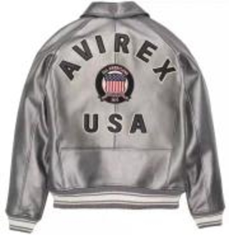 Puede incluir: Chaqueta bomber plateada con el texto "AVIREX USA" bordado en la espalda. La chaqueta presenta un dise&ntilde;o cl&aacute;sico con cuello, pu&ntilde;os y dobladillo de canal&eacute;. La chaqueta tiene un brillo met&aacute;lico y un parche con la bandera americana.