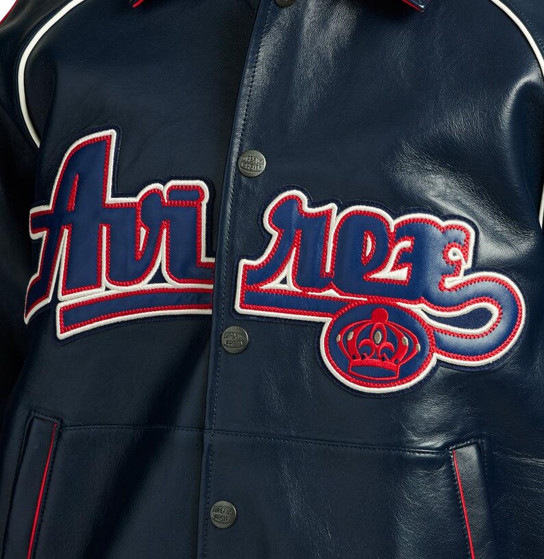 Puede incluir: Chaqueta universitaria azul marino con detalles blancos y rojos. La chaqueta presenta la palabra "Ari Roes" en una fuente estilizada, con un emblema de corona. Tiene cierre de botones y cuello cl&aacute;sico.