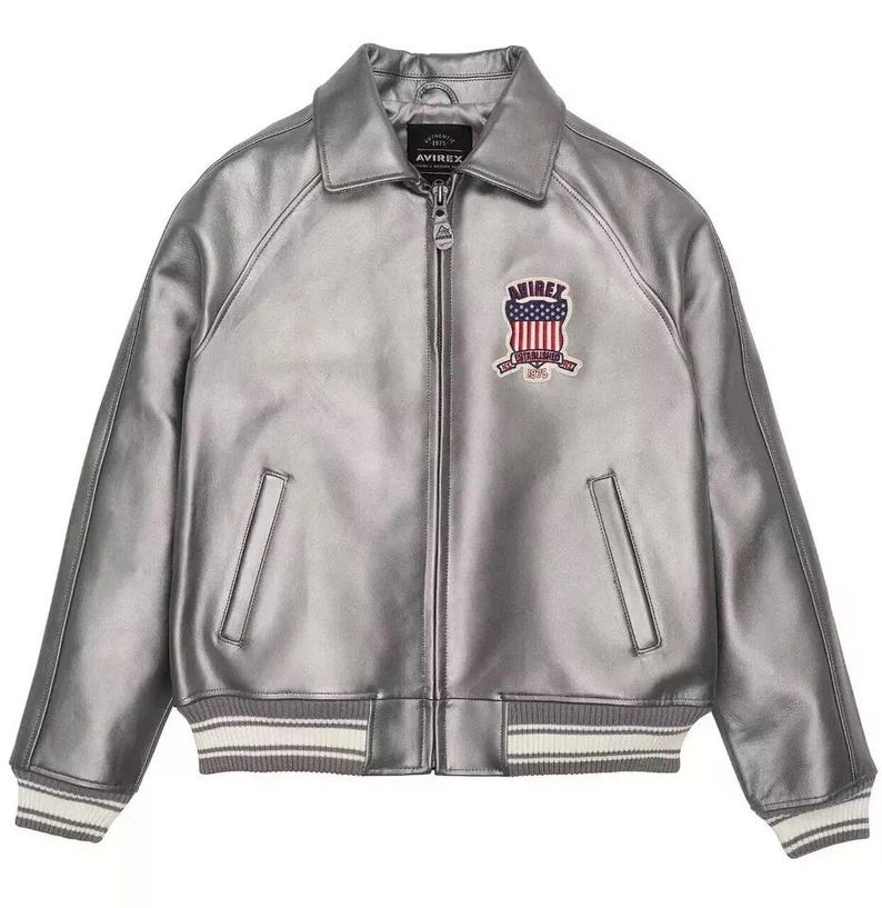 Puede incluir: Chaqueta de cuero plateada con cremallera, cuello y pu&ntilde;os acanalados con rayas blancas. Cuenta con un parche en el pecho con un dise&ntilde;o de bandera americana y el nombre de la marca. Un estilo cl&aacute;sico de chaqueta bomber.