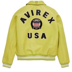 May include: A chartreuse leather jacket with the word "AVIREX" arched across the upper back in black block letters. Below the word "AVIREX" is a circular patch with the words "ALL AMERICANS" and "ESTABLISHED 1975". The word "USA" is below the patch.