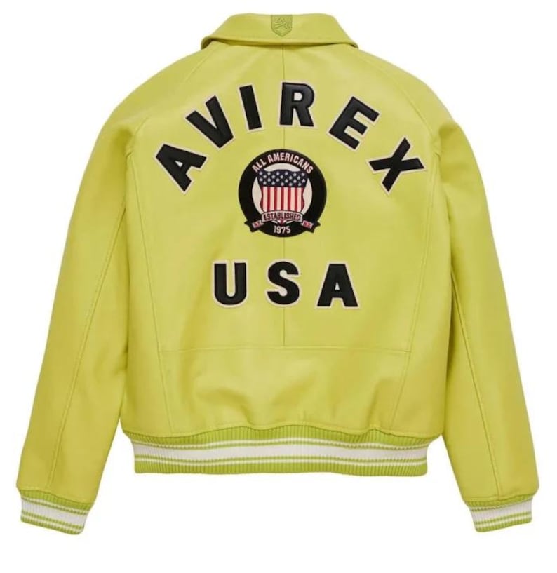 May include: A chartreuse leather jacket with the word "AVIREX" arched across the upper back in black block letters. Below the word "AVIREX" is a circular patch with the words "ALL AMERICANS" and "ESTABLISHED 1975". The word "USA" is below the patch.