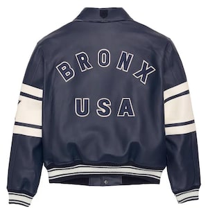 May include: Navy blue leather jacket with white detailing and the text "BRONX USA" arched across the back. The jacket has white stripes on the sleeves and a ribbed hem. A classic varsity style.