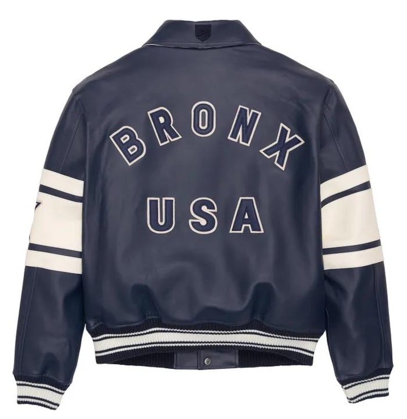 May include: Navy blue leather jacket with white detailing and the text "BRONX USA" arched across the back. The jacket has white stripes on the sleeves and a ribbed hem. A classic varsity style.