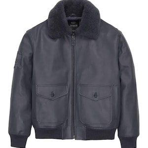 May include: A dark gray leather bomber jacket with a faux fur collar. The jacket features two front pockets, a zipper closure, and a patch on the left sleeve. The jacket has a ribbed hem and cuffs.