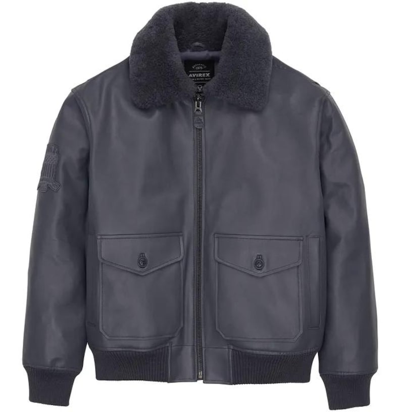 May include: A dark gray leather bomber jacket with a faux fur collar. The jacket features two front pockets, a zipper closure, and a patch on the left sleeve. The jacket has a ribbed hem and cuffs.