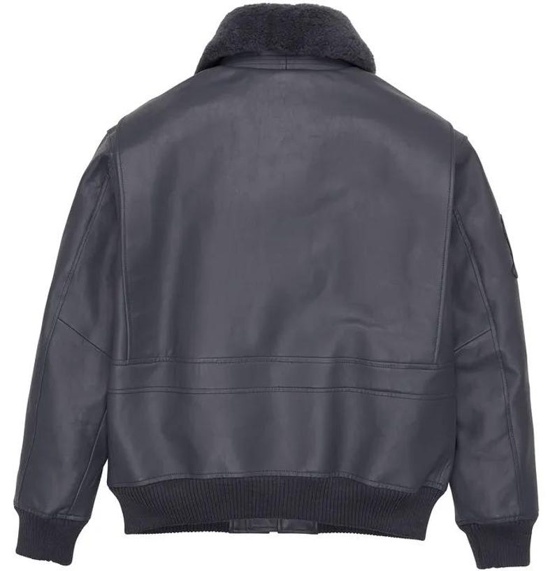 May include: A dark navy blue leather bomber jacket with a shearling collar. The jacket features a ribbed knit hem and cuffs, and a patch on the upper left sleeve. The back view shows the jacket's design details.