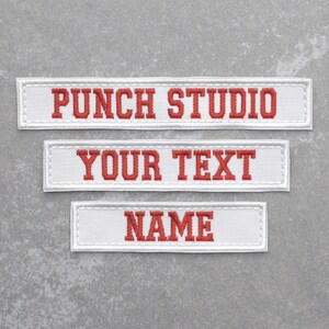May include: Three white fabric patches with red embroidered text. The top patch reads "PUNCH STUDIO", the middle patch reads "YOUR TEXT", and the bottom patch reads "NAME".