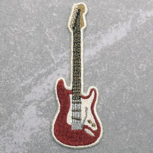May include: Red electric guitar with a white pickguard and a brown neck. The guitar is embroidered on a white fabric.