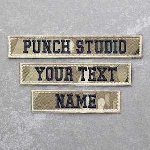 May include: Three tan and brown camouflage fabric name tags with black stitching. The top tag reads "PUNCH STUDIO", the middle tag reads "YOUR TEXT", and the bottom tag reads "NAME".