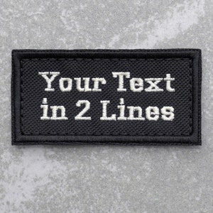 May include: Black rectangular patch with white embroidered text that reads "Your Text in 2 Lines".