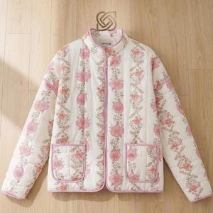 May include: A quilted jacket with a floral pattern in pink and peach on a white background. The jacket has a stand-up collar, two front pockets, and a light pink trim. The brand name "THTREME" is printed on the collar.