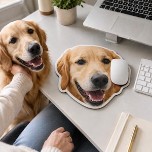 Op de afbeelding: Een op maat gevormde muismat met een fotografische print in hoge resolutie van het gezicht van een golden retriever met een glimlachende uitdrukking. De muismat ligt op een bureau naast een witte computermuis, een laptop en een notitieblok.