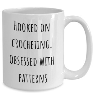 May include: White ceramic coffee mug with black text that reads "Hooked on crocheting, obsessed with patterns".