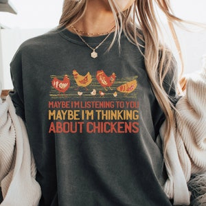 May include: A dark gray t-shirt with a graphic of chickens and the text "Maybe I'm listening to you, maybe I'm thinking about chickens".