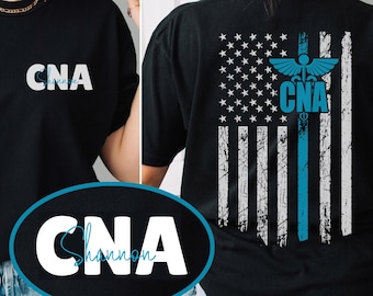 Op de afbeelding: Zwart T-shirt met een blauw-wit Amerikaans vlagontwerp met een medisch caduceussymbool en de tekst "CNA". De voorkant van het shirt heeft de tekst "CNA" met de naam "Shannon" eronder.