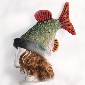 May include: A novelty fish-shaped hat in green, grey, and yellow, with red and orange fins. The hat, made of felted wool, features a black brim. This unique hat is designed to be worn on the head, offering a quirky accessory.