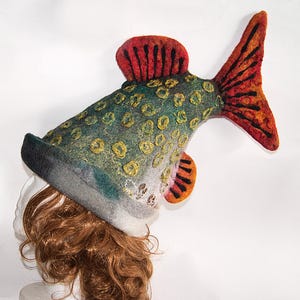 May include: A novelty fish-shaped hat in green, grey, orange, and red. The felt hat has a detailed design with scales and fins. This unique accessory is suitable for costume parties or themed events. The hat is a fun and quirky fashion statement.