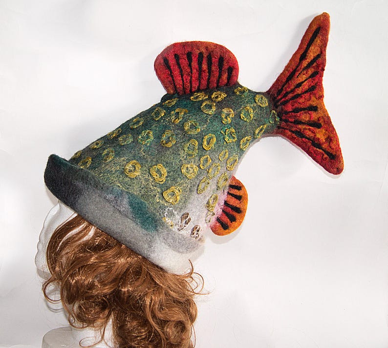 May include: A novelty fish-shaped hat in green, grey, orange, and red. The felt hat has a detailed design with scales and fins. This unique accessory is suitable for costume parties or themed events. The hat is a fun and quirky fashion statement.