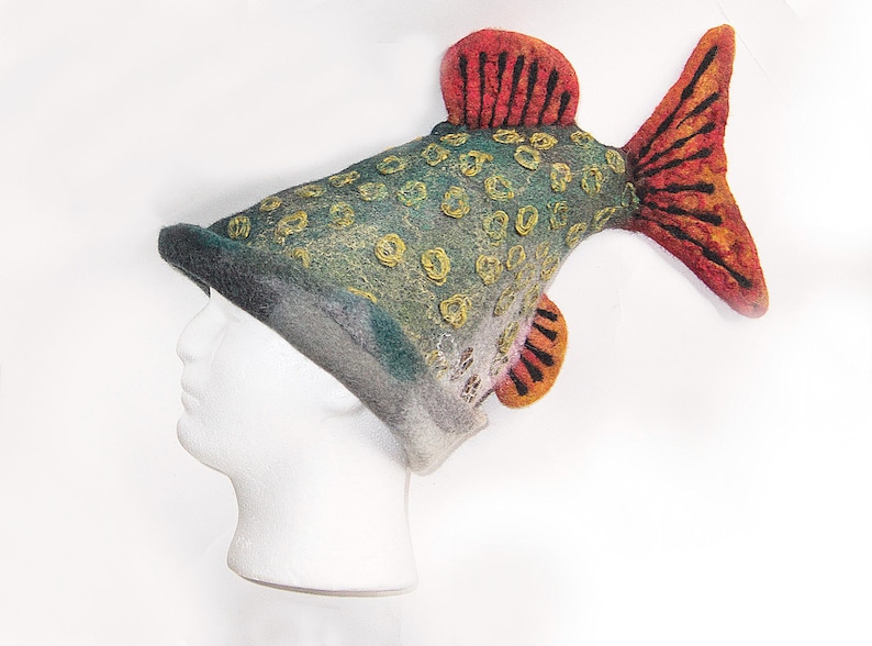 May include: A novelty fish-shaped hat in green, yellow, orange, and red felt. The hat has detailed fins and scales, and is displayed on a white mannequin head. The hat's design is eye-catching and unique.