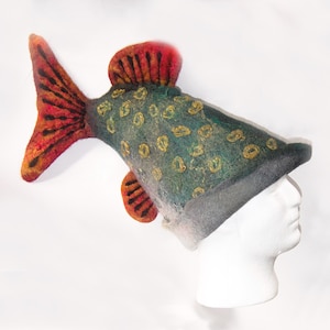 May include: A novelty fish-shaped hat made from felt. The hat features a tail and fins in shades of red and orange, with a teal body decorated with yellow spots. The hat is designed to be worn on the head, offering a playful accessory.