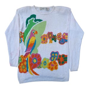 Può includere: Maglione bianco con un motivo colorato di pappagallo e fiori. Il pappagallo presenta piume rosa, gialle, blu e arancioni, con uno sfondo verde. I fiori sono arancioni, gialli e blu. Il maglione ha maniche lunghe.