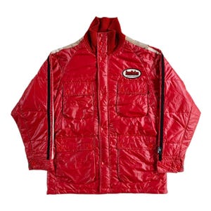 May include: A vibrant red quilted jacket with a high collar and several pockets. The jacket has black stripes on the sleeves and a small patch with text. The jacket has a shiny, reflective finish.