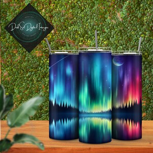 Pode incluir: Tr&ecirc;s copos de a&ccedil;o inoxid&aacute;vel com um design de aurora boreal refletido em um lago. Os designs apresentam cores diferentes e elementos celestiais, incluindo uma estrela cadente, uma lua crescente e uma lua cheia.
