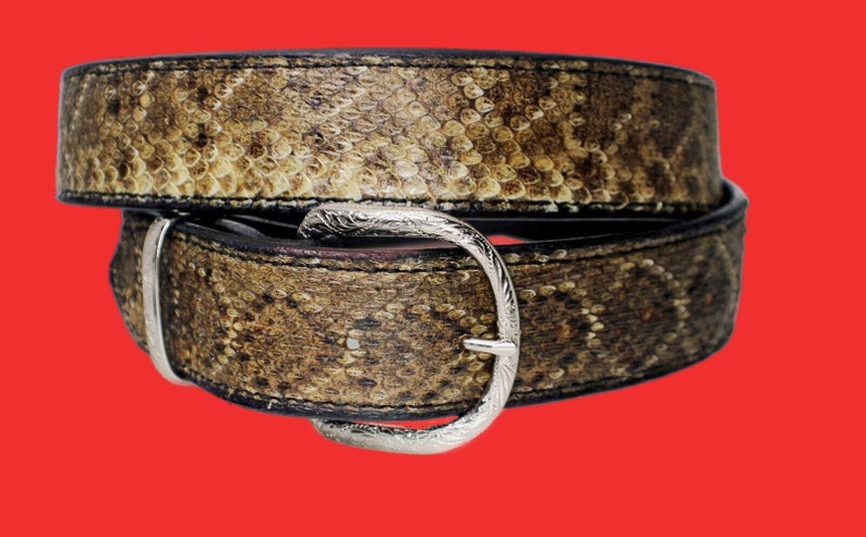 K&ouml;nnte beinhalten: Ein brauner Lederg&uuml;rtel mit einer silbernen Schnalle. Der G&uuml;rtel ist aus Schlangenleder und hat ein strukturiertes Muster.