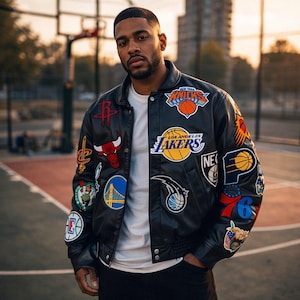 Puede incluir: Chaqueta de cuero negra con múltiples parches de logotipos de equipos, incluidos los New York Knicks y Los Angeles Lakers. La chaqueta tiene dobladillo y puños acanalados. La persona está de pie en una cancha de baloncesto.