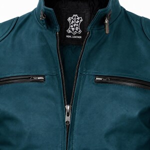 K&ouml;nnte beinhalten: Eine petrolfarbene Lederjacke mit Stehkragen, einem zentralen Metallrei&szlig;verschluss und zwei horizontalen Brusttaschen mit schwarzen Rei&szlig;verschl&uuml;ssen. Das Innenetikett zeigt ein fellf&ouml;rmiges Logo mit dem Schriftzug REAL LEATHER in Wei&szlig;.