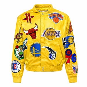 Puede incluir: Una chaqueta bomber de satén amarillo brillante con una variedad de logotipos de equipos de la NBA y gráficos de baloncesto bordados en la parte delantera y las mangas. La chaqueta incluye cuello, cierre frontal con botones y puños acanalados.