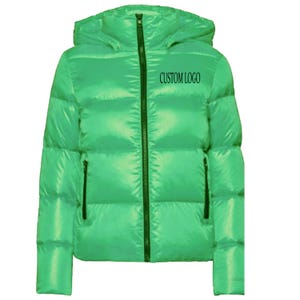 Può includere: Giacca puffer verde brillante con cappuccio e cerniera nera. Presenta due tasche laterali con cerniere nere e la scritta "CUSTOM LOGO". Giacca imbottita per climi freddi.