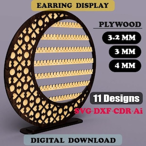 Pode incluir: Um expositor de brincos de madeira castanha escura em forma de meia-lua, com recortes de coração e várias filas de ranhuras para brincos. O texto "EARRING DISPLAY", "PLYWOOD", "11 Designs" e "DIGITAL DOWNLOAD" são visíveis.