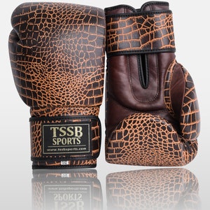 May include: A pair of brown and orange boxing gloves with a crocodile skin pattern. The gloves have black straps and a gold logo that reads "TSSB SPORTS" and "www.tssbsports.com".