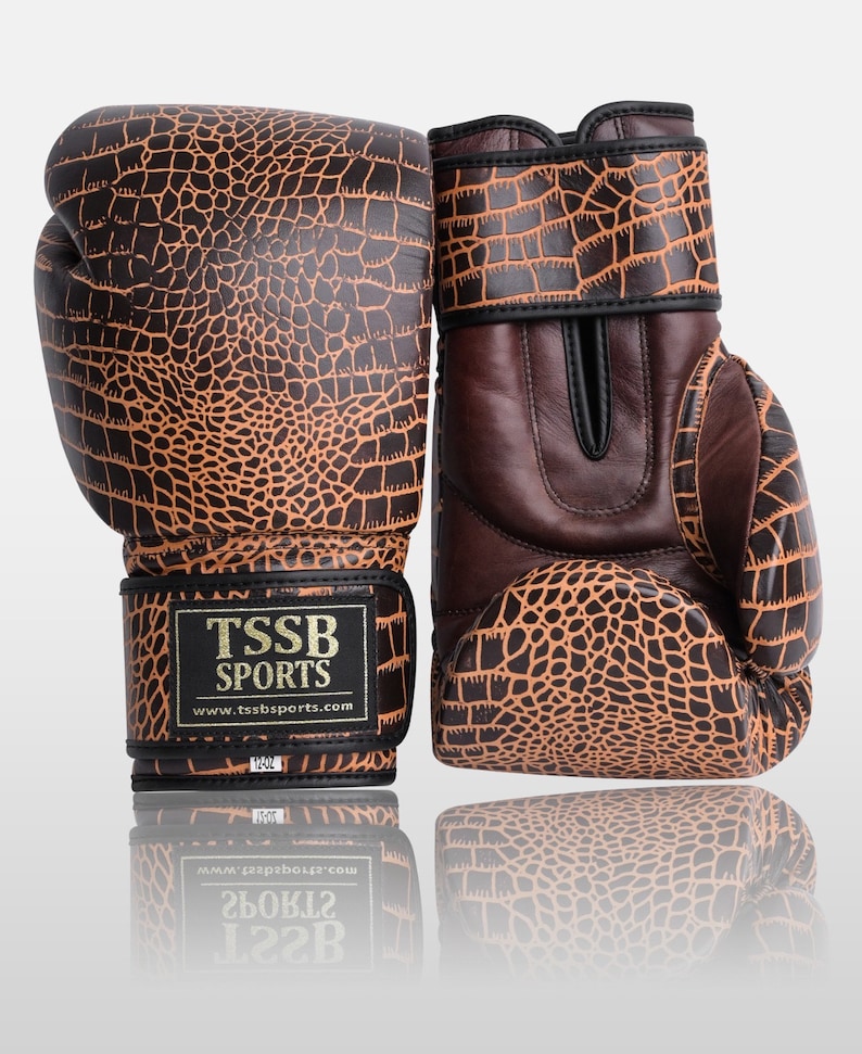 May include: A pair of brown and orange boxing gloves with a crocodile skin pattern. The gloves have black straps and a gold logo that reads "TSSB SPORTS" and "www.tssbsports.com".
