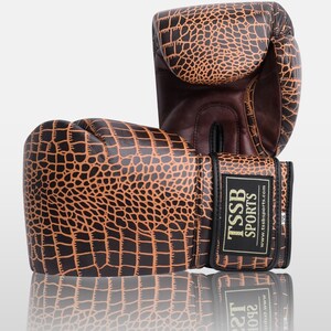 May include: A pair of brown and black boxing gloves with a crocodile skin pattern. The gloves have a black strap with the text "TSSB SPORTS" and "www.tssbsports.com" printed on it.