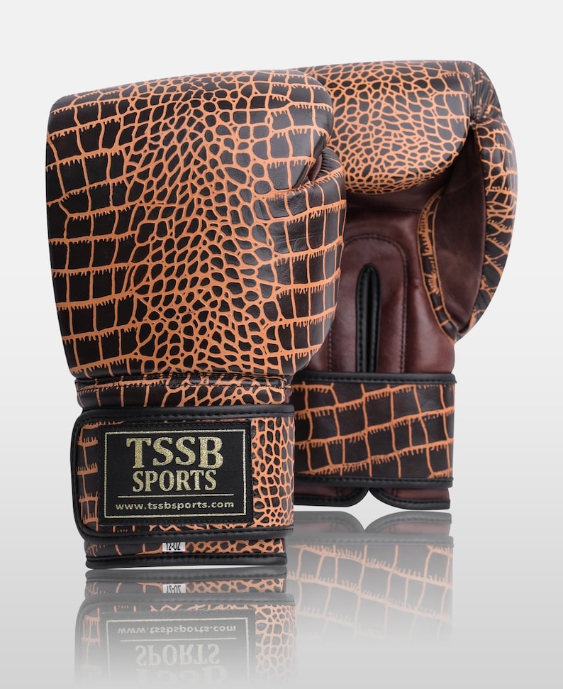 May include: A pair of brown and black boxing gloves with a crocodile skin pattern. The gloves have a black strap with the text "TSSB SPORTS" and the website "www.tssbsports.com".